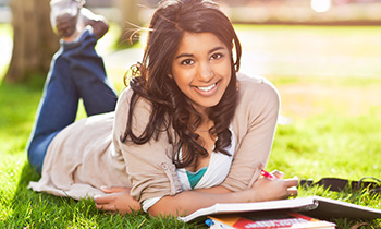 Young woman laying in the grass with study materials.
